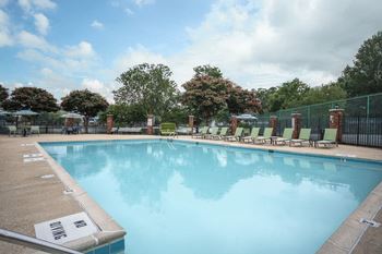 A large swimming pool surrounded by a fence and lounge chairs.